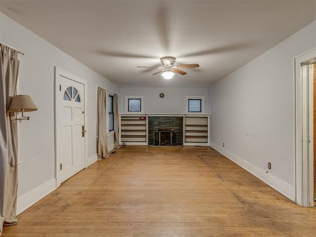 unfurnished living room featuring ceiling fan, baseboards, light wood finished floors, and a fireplace