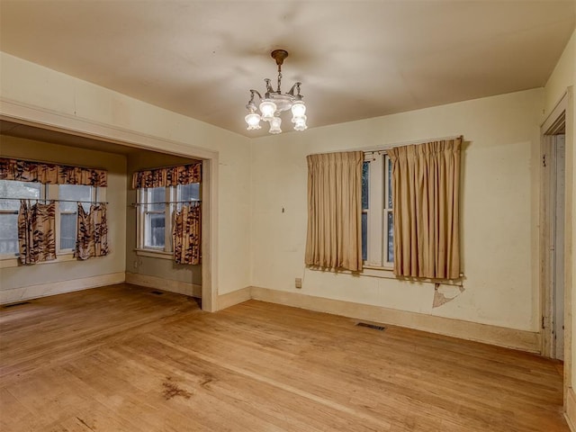spare room with a chandelier, baseboards, visible vents, and light wood-style flooring