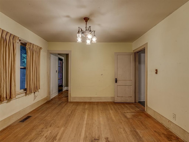 empty room featuring baseboards, visible vents, light wood finished floors, and a chandelier