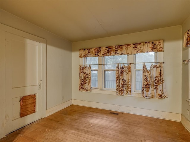 empty room with a healthy amount of sunlight, baseboards, wood finished floors, and visible vents
