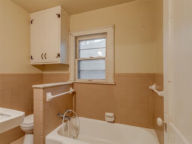 bathroom with toilet, tile walls, wainscoting, and a tub to relax in
