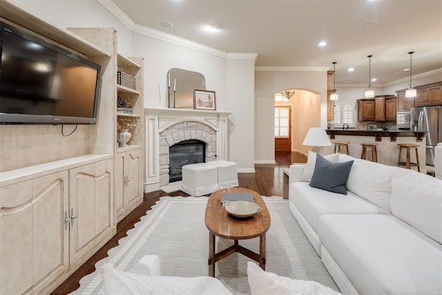 living room with a fireplace, wood finished floors, crown molding, and arched walkways
