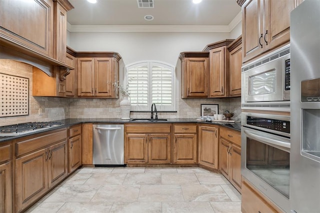 kitchen featuring decorative backsplash, crown molding, a sink, stainless steel appliances, and brown cabinetry