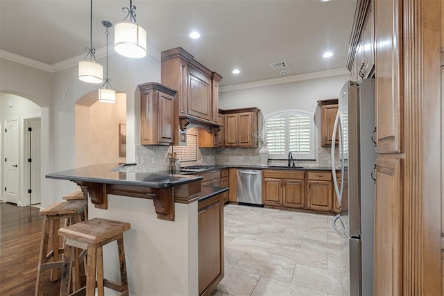 kitchen featuring a sink, appliances with stainless steel finishes, dark countertops, arched walkways, and a peninsula