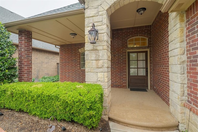 doorway to property with brick siding and roof with shingles