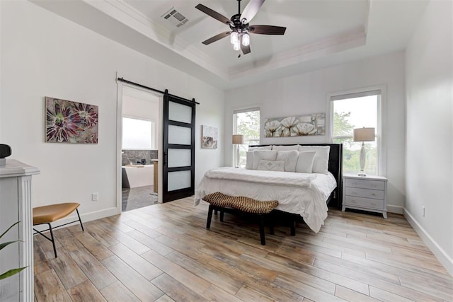 bedroom with a raised ceiling, light wood-style floors, visible vents, a barn door, and ornamental molding