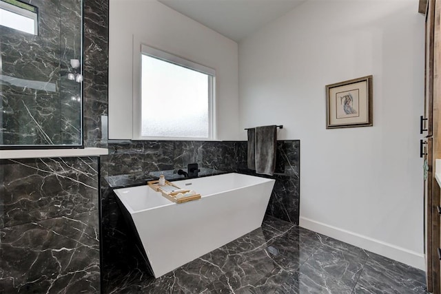 full bath with plenty of natural light, a freestanding bath, marble finish floor, and baseboards