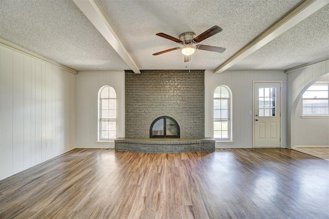 unfurnished living room featuring beam ceiling, a brick fireplace, a textured ceiling, and wood finished floors