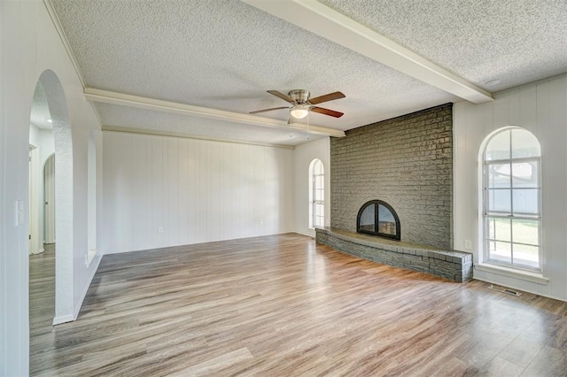 unfurnished living room featuring a ceiling fan, a textured ceiling, arched walkways, a brick fireplace, and wood finished floors