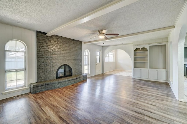 unfurnished living room featuring arched walkways, a textured ceiling, a brick fireplace, and wood finished floors