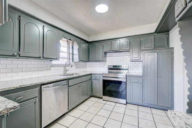 kitchen featuring light stone countertops, appliances with stainless steel finishes, a sink, a textured ceiling, and tasteful backsplash