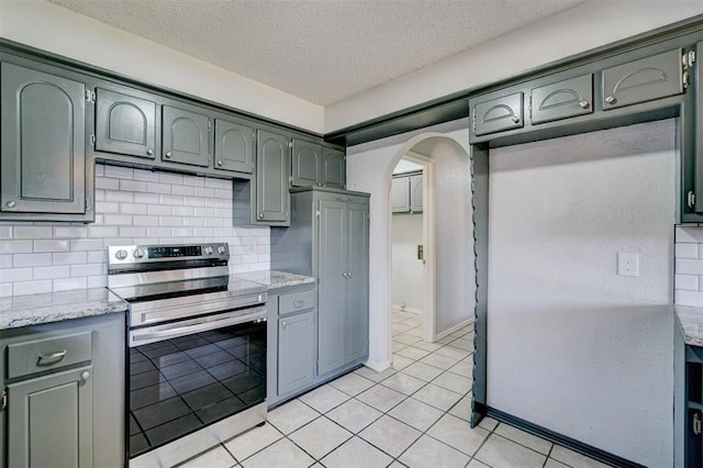 kitchen featuring a textured ceiling, arched walkways, backsplash, light tile patterned floors, and stainless steel range with electric cooktop