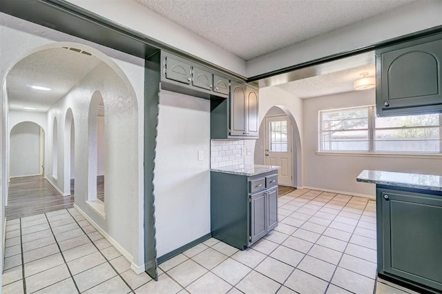kitchen with a textured ceiling, light tile patterned floors, arched walkways, backsplash, and gray cabinetry