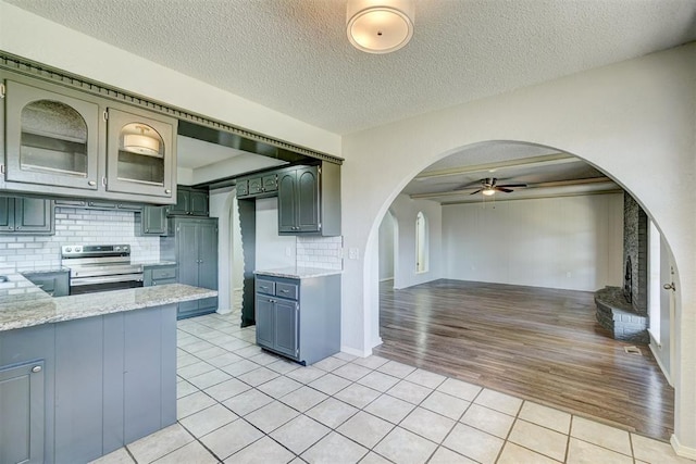 kitchen with a ceiling fan, open floor plan, electric stove, arched walkways, and light tile patterned floors