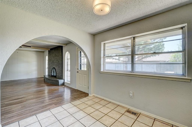 entrance foyer featuring visible vents, a brick fireplace, a textured ceiling, arched walkways, and light tile patterned floors