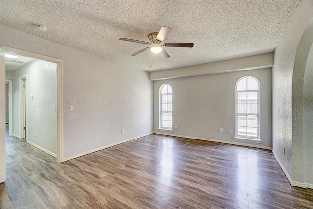 unfurnished room with a ceiling fan, a textured wall, wood finished floors, and a textured ceiling