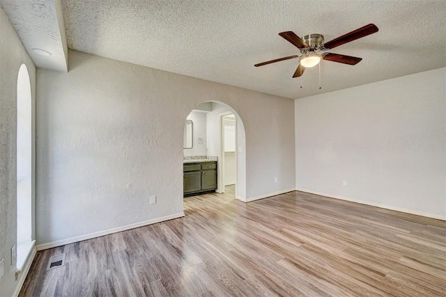 empty room with ceiling fan, a textured ceiling, visible vents, arched walkways, and light wood-style floors