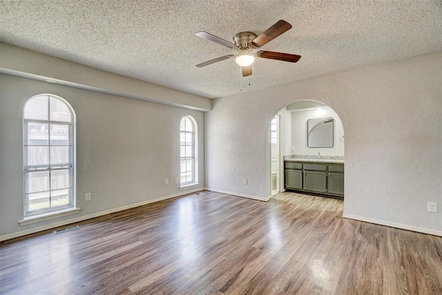 spare room featuring arched walkways, a textured ceiling, ceiling fan, and wood finished floors