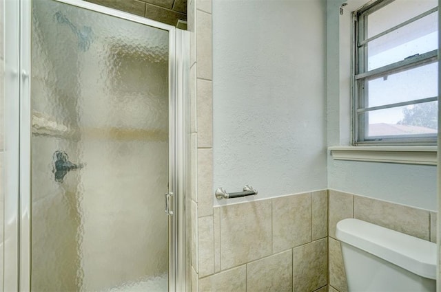 bathroom with tile walls, a textured wall, a stall shower, and toilet