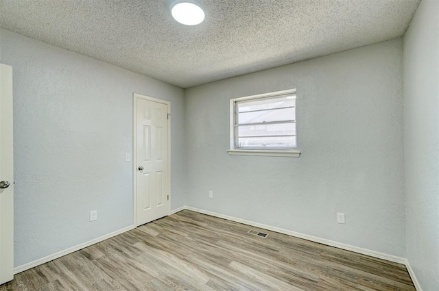 empty room with visible vents, baseboards, a textured ceiling, and wood finished floors