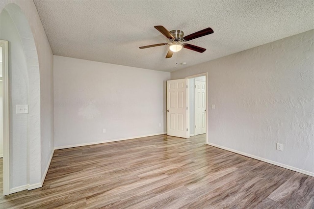 spare room with wood finished floors, baseboards, a textured ceiling, arched walkways, and a ceiling fan