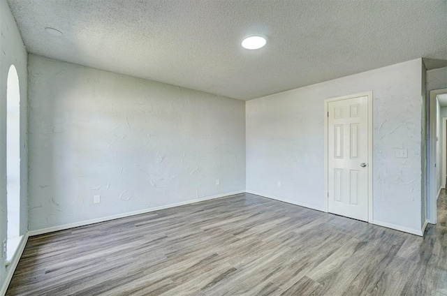 empty room with baseboards, a textured ceiling, and wood finished floors