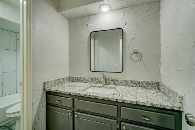 full bath featuring toilet, a textured wall, a bathtub, and vanity