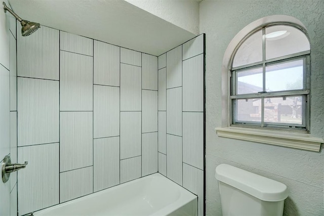 bathroom with a textured wall, toilet, and tub / shower combination