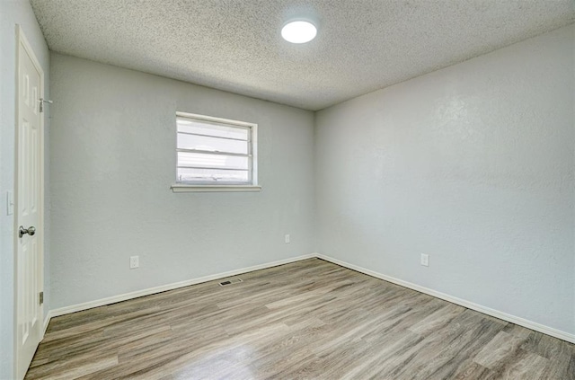 spare room with baseboards, a textured ceiling, visible vents, and wood finished floors