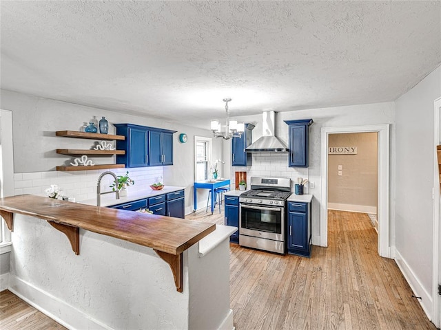 725 NE 15th St, Oklahoma City, OK 73104 - kitchen featuring open shelves, blue cabinets, stainless steel range with gas stovetop, wall chimney exhaust hood, and a notable chandelier