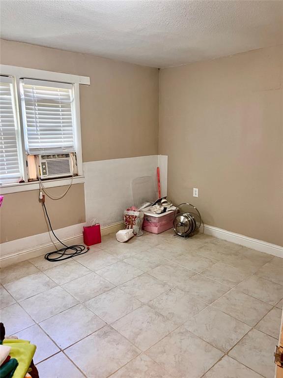 607 E Liveoak St, Altus, OK 73521 - spare room featuring a textured ceiling, cooling unit, and light tile patterned flooring