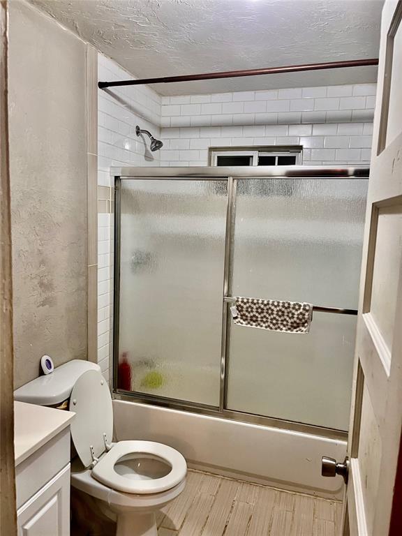 607 E Liveoak St, Altus, OK 73521 - full bathroom featuring combined bath / shower with glass door, vanity, and a textured ceiling