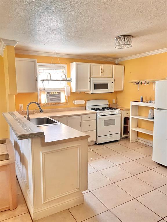 607 E Liveoak St, Altus, OK 73521 - kitchen with white appliances, a peninsula, crown molding, a textured ceiling, and light tile patterned floors