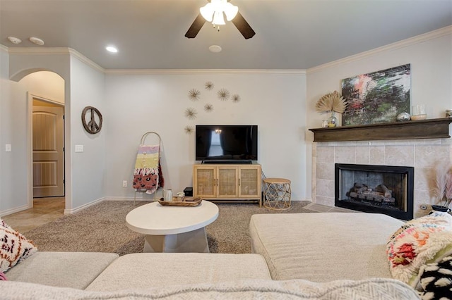 15808 Cantera Creek Dr, Edmond, OK 73013 - carpeted living room featuring crown molding, ceiling fan, baseboards, arched walkways, and a tiled fireplace