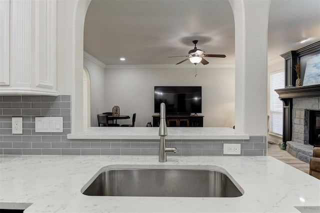 2051 Vaquero Ct, Edmond, OK 73034 - kitchen featuring light stone counters, a ceiling fan, ornamental molding, a sink, and arched walkways
