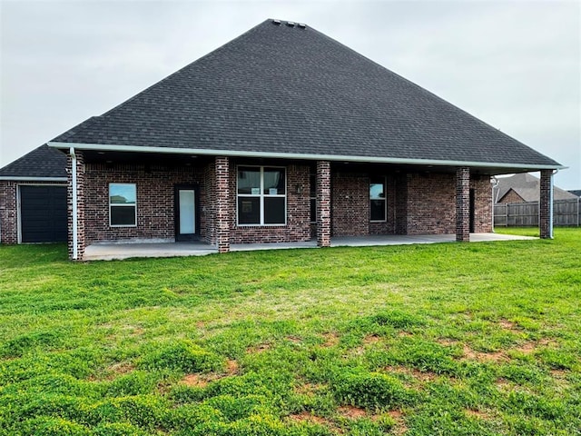 back of house featuring brick siding, a patio area, roof with shingles, and a lawn