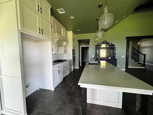 kitchen with oven, visible vents, a sink, a spacious island, and white cabinetry