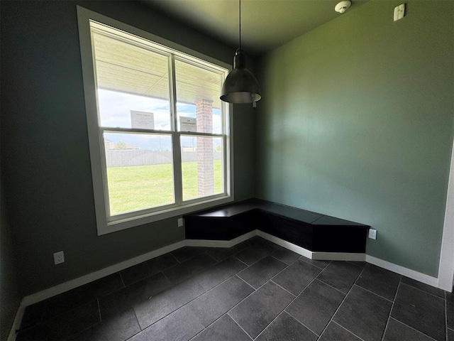 unfurnished dining area featuring baseboards and dark tile patterned floors