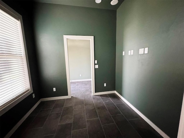 unfurnished room with dark tile patterned floors and baseboards