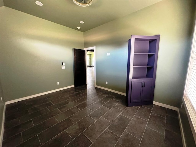 unfurnished room with baseboards, vaulted ceiling, and dark tile patterned flooring