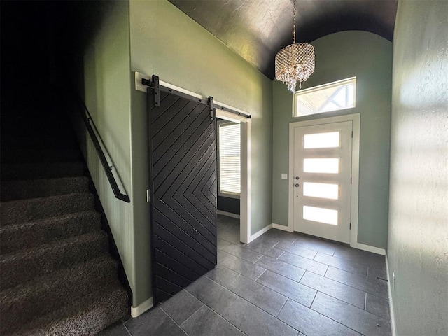 foyer entrance featuring vaulted ceiling, an inviting chandelier, a barn door, and dark tile patterned flooring