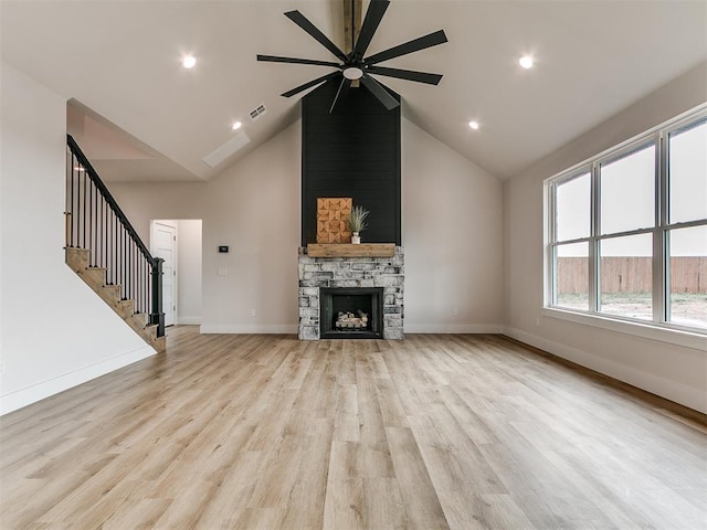 unfurnished living room featuring baseboards, a stone fireplace, light wood finished floors, ceiling fan, and stairway