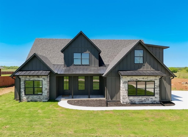 back of house with a lawn, board and batten siding, roof with shingles, and stone siding
