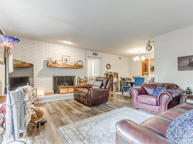 living room with an inviting chandelier, a brick fireplace, wood finished floors, and visible vents