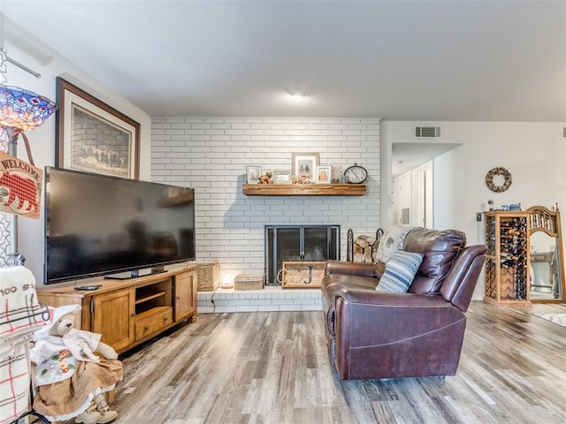 living room with visible vents, light wood finished floors, and a brick fireplace