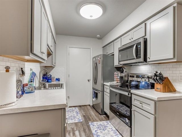 kitchen with a sink, light countertops, stainless steel appliances, light wood-type flooring, and backsplash