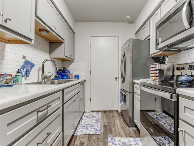 kitchen featuring backsplash, a sink, light countertops, light wood finished floors, and stainless steel appliances