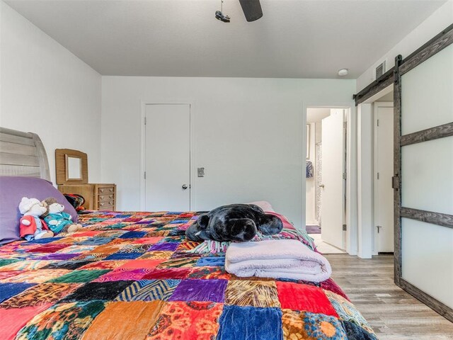 bedroom with ceiling fan, visible vents, a barn door, and light wood-style flooring