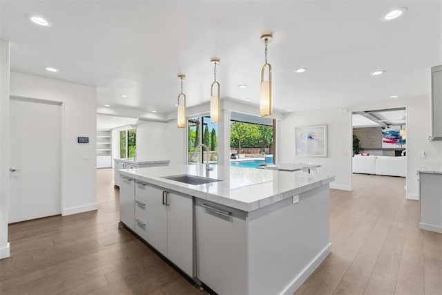 kitchen with baseboards, open floor plan, a center island with sink, recessed lighting, and a sink
