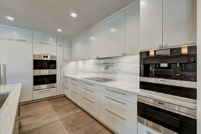 kitchen with light stone counters, stainless steel appliances, light wood-type flooring, and a warming drawer